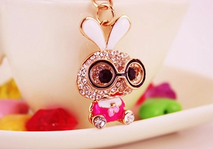 Close-up of sparkling rhinestone bunny keychain with glasses next to a white ceramic cup