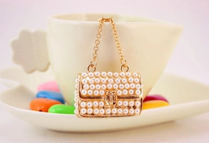 Close-up of a mini pearl handbag charm with gold chain on a white coffee cup rim