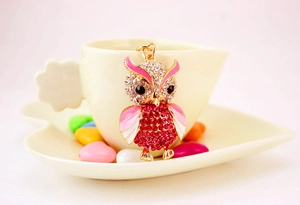 Detail of owl keychain with rose pink crystals and enamel finish on a beige cup