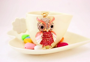 Detailed macro of golden owl keychain with pink rhinestones on a white cup