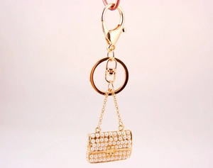 Detailed close-up of golden keychain with white pearl mini handbag charm and lobster clasp