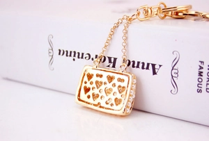 Detail shot of golden handbag keychain with hollow hearts and pearls on a white book