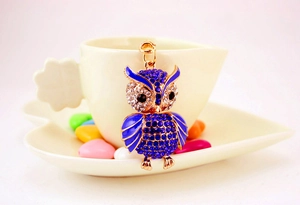 Detailed shot of an owl keychain with blue rhinestones hanging on a white ceramic cup