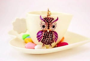 Close-up of golden owl keychain with purple crystals on a ceramic coffee cup