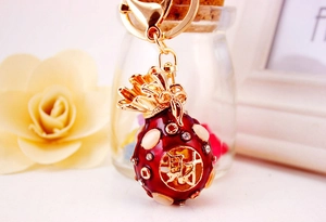 Detail of fortune bag keychain with red enamel, crystal inlay and Chinese character Cai