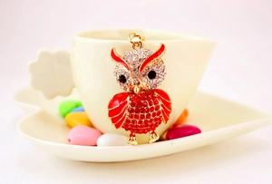 Detail of owl pendant keychain with red crystals and gold finish on ceramic cup