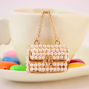 Miniature pearl-studded handbag keychain with gold chain on a porcelain cup