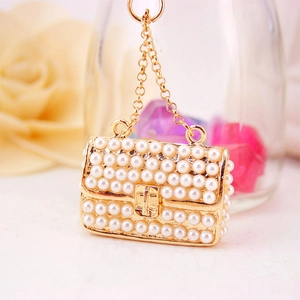 Elegant gold pearl handbag keychain charm with white pearl embellishment on floral background