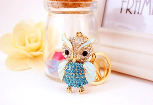 Macro detail of golden owl keychain with blue crystals and soft enamel finish