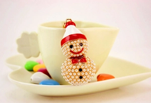 Dettaglio portachiavi pupazzo di neve in perle con cappello rosso su tazzina da caffè
