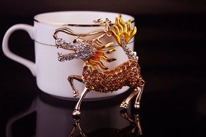 Detailed macro view of a golden Kirin keychain with amber rhinestones on a white porcelain cup