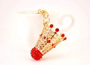 Détail d'un porte-clés badminton doré avec cristaux rouges près d'une tasse blanche