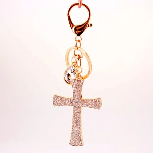 Porte-clés croix dorée avec cristaux goutte d'eau et fermoir mousqueton sur fond rose pastel