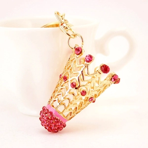 Porte-clés couronne dorée avec strass roses présenté sur une tasse en céramique blanche