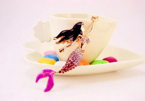 Détail d'un porte-clés sirène en strass violets suspendu sur une tasse à café blanche