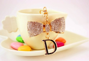 Détail du porte-clés nœud doré avec strass brillants et pendentif lettre D noire