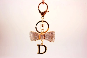 Vue détaillée du nœud en strass et pendentif lettre D sur porte-clés en métal doré