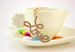 Detailed close-up of golden Love letter keychain with rhinestones on a ceramic cup