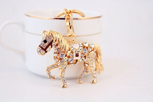 Vue détaillée d'un porte-clés cheval doré avec cristaux et émail sur une tasse blanche