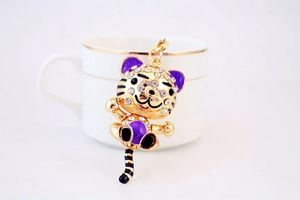 Porte-clés tigre en émail violet et strass blancs, gros plan sur une table blanche