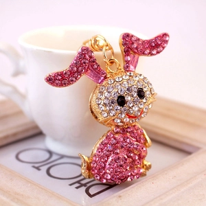 Pink and white rhinestone bunny keychain with gold alloy finish on a white ceramic cup