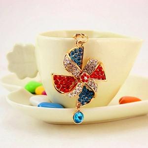 Golden windmill car keychain with colorful rhinestones hanging on a ceramic cup edge