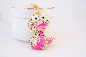 Détail d'un porte-clés serpent rose avec cadre doré et cristaux blancs sur une tasse