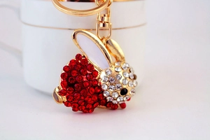 Makroaufnahme von rotem Strass-Hasen-Schlüsselanhänger mit goldenem Ring an weißer Tasse