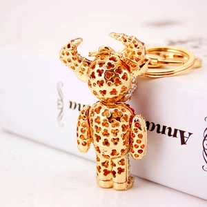 Golden bear keychain with devil horns, clover cutouts and rhinestones on white books