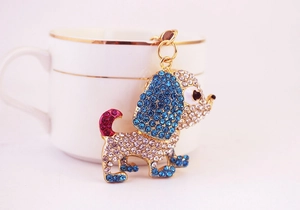 Dettaglio di un ciondolo a forma di cane con strass blu, bianchi e rosa su gancio oro