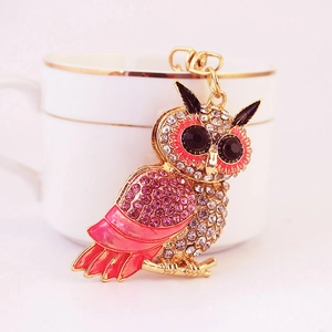 Sparkly pink owl keychain with crystals and gold finish on a white ceramic background