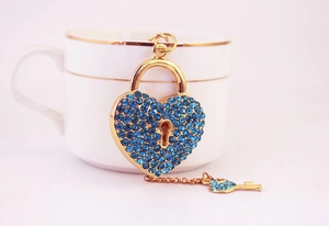 Détail d'un pendentif cadenas en forme de cœur doré avec strass bleu roi et sa petite clé