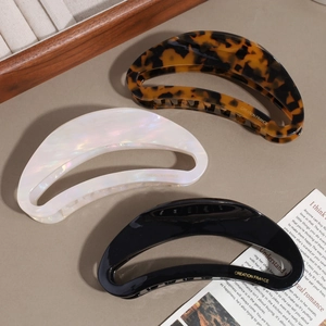 Detailed macro view of large acetate crescent hair claws in tortoise, pearl, and black finishes