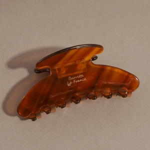 Detailed view of acetate hair claw clip in dark amber tortoise shell finish with gold text