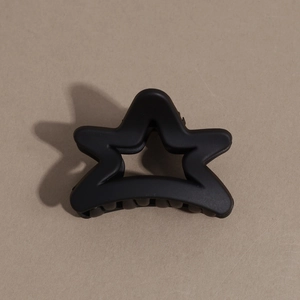 Detailed macro view of a matte black star-shaped hair claw clip on a brown surface