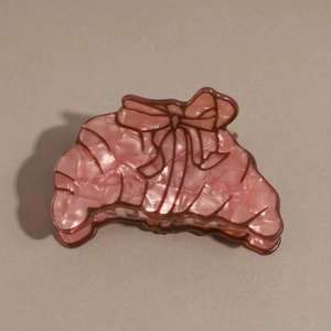 Detailed close-up of a pink croissant hair claw clip with marble texture and bow print