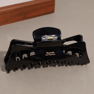 Close-up of a glossy black hair claw clip with golden text and metal spring detail
