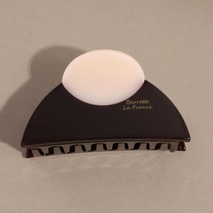 Detail of semicircular acetate hair claw clip in dark brown with gold brand lettering
