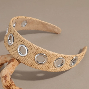 Detail of raffia woven headband with silver metal eyelets on a natural wood stand