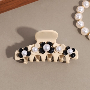 Detailed view of cream resin hair claw clip with floral pearl accents on a khaki surface