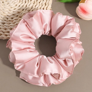 Close-up of pink satin scrunchie with soft waves and silky texture on a neutral background