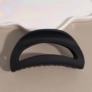 Detail of a large matte black hair claw clip resting on a white pearlescent cloud tray