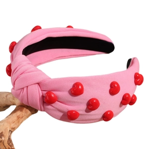 Pink knotted wide headband with red heart ornaments on natural wooden branch background