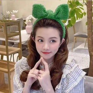 Detail of a plush green bow headband for face washing worn by a model in a cozy cafe