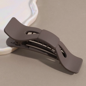 Detail view of large matte coffee brown bow-shaped claw clip with wave-shaped hollow design