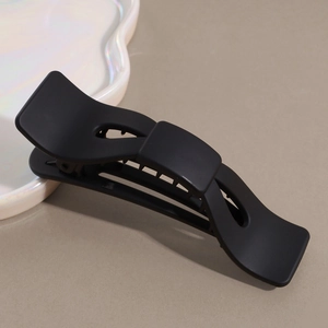 Detail shot of a sleek matte black bow hair clip on a minimalist decorative tray