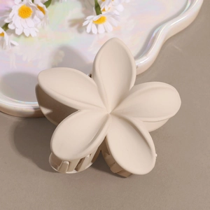 Detail of matte cream flower hair claw clip on a decorative tray with small daisies