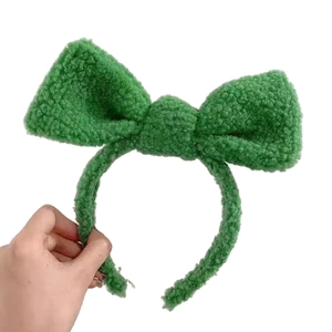 Hand holding a cute green fleece bow headband for women with soft lamb wool texture