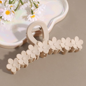 Close-up of cream matte plumeria hair claw clip with floral details on soft gray surface