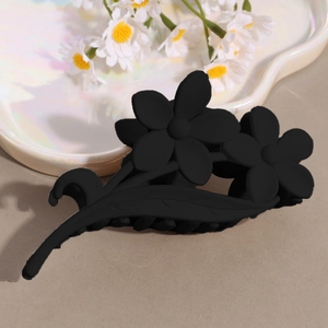 Detail of matte black floral hair claw clip on heart-shaped pearl tray with daisy flowers
